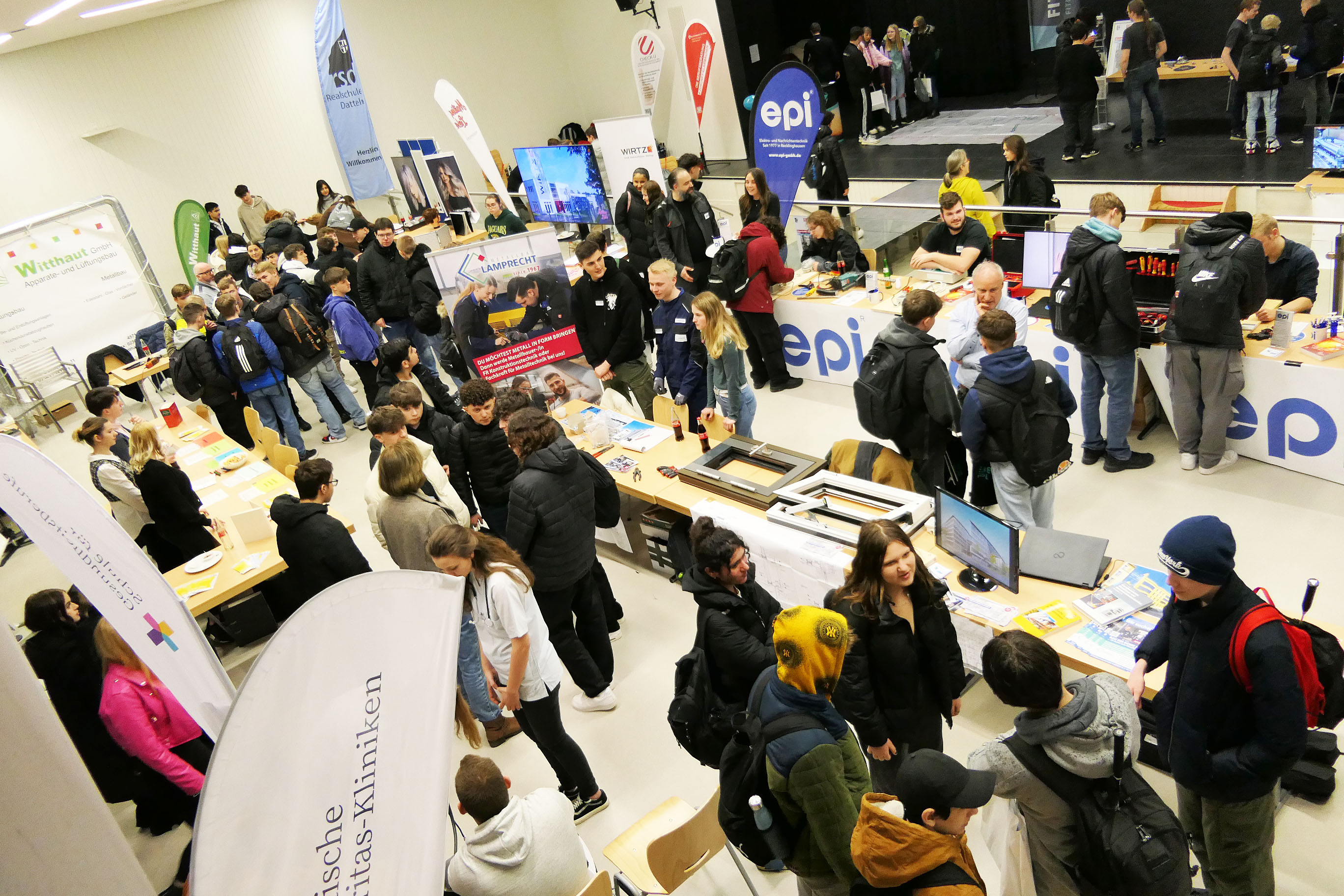 Das Bild zeigt Unternehmen in der Aula der Realschule, die sich auf der Ausbildungsmesse F1rst Job - First Contact Schüler*innen vorgestellt haben.