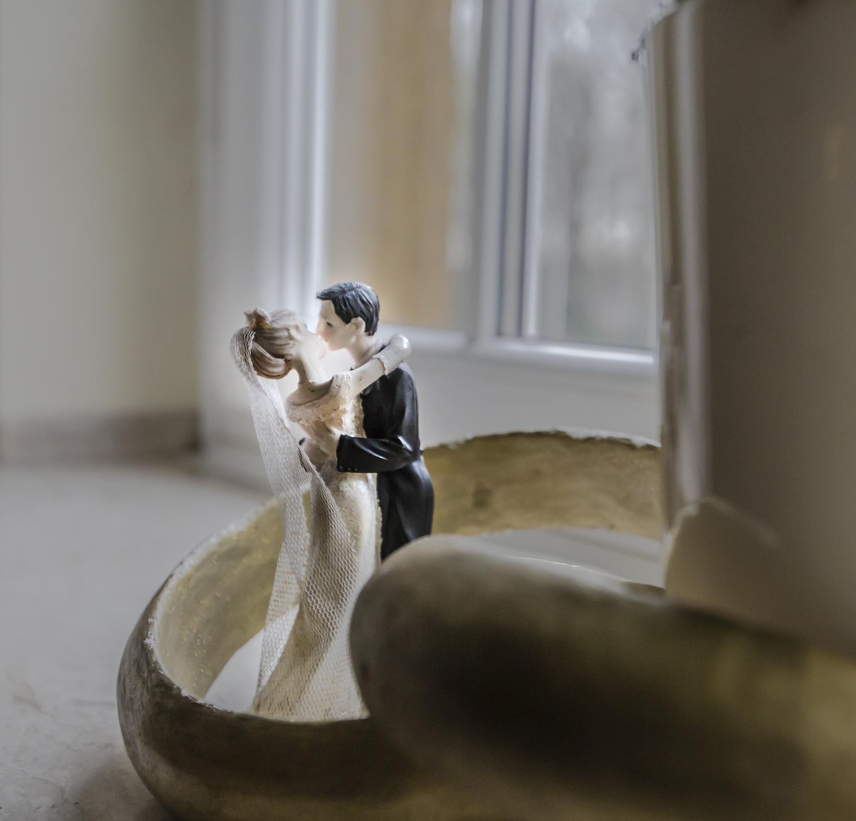 Das Bild zeigt zwei kleine Figuren, die ein Brautpaar darstellen sollen, die sich in einem überdimensionalen Ehering umarmen