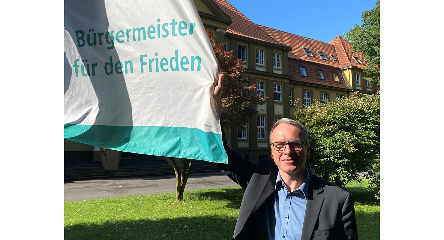 Bürgermeister André Dora zeigt die Mayors-for-Peace-Flagge vor dem Rathaus