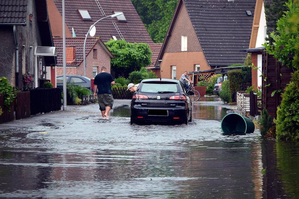 Überschwemmte Straße im Beisenkamp. In der Mitte Steht ein Auto komplett im Wasser, der Fahrer schaut auf dem Fenster. Daneben steht ein Mann.