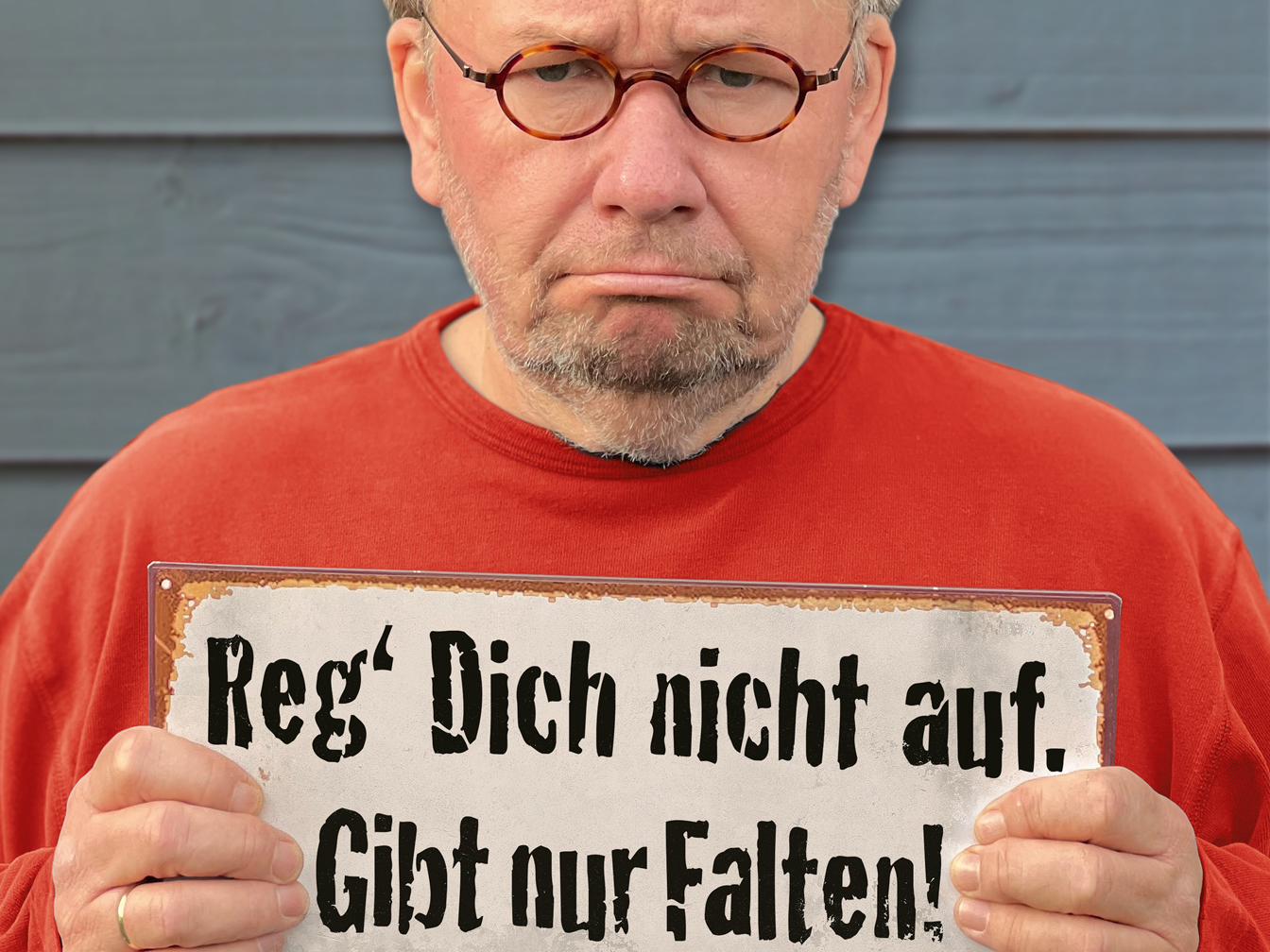 Bernd Stelter mit einem Schild "Reg dich nicht auf, gibt nur Falten!