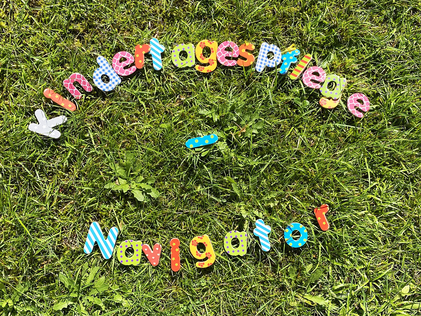 Das Wort "Kindertagespflege-Navigator" ist mit einzelnen bunten Buchstaben auf einem Rasen gelegt worden.
