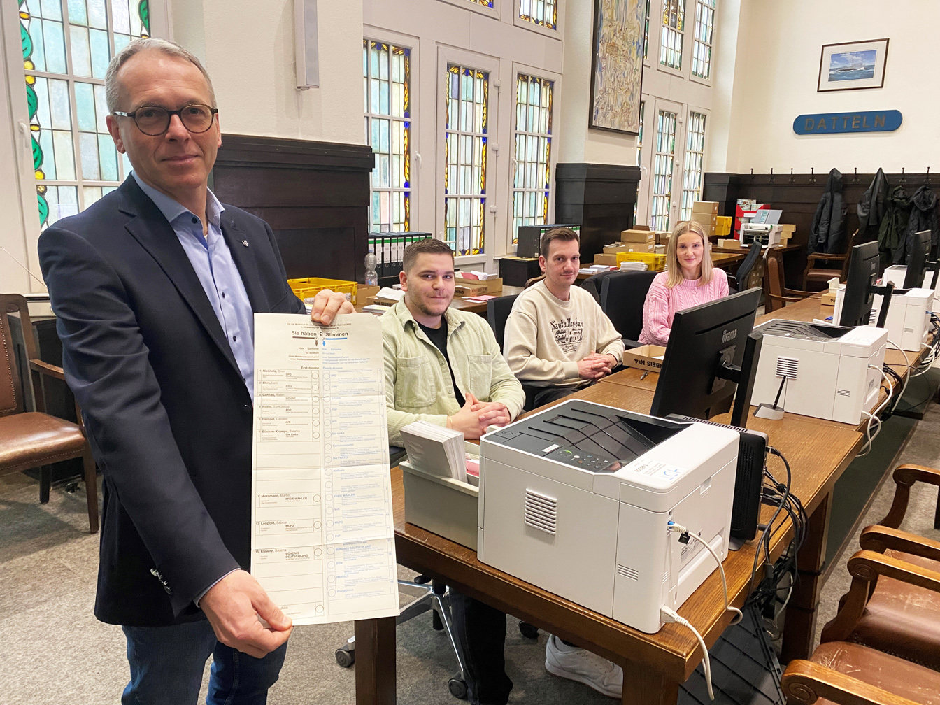 Bürgermeister André Bürgermeister mit einem Stimmzettel für die Bundestagswahl – daneben vom Wahlamt Alexander Pepping, Veith Gale und Svenja Milevskij.