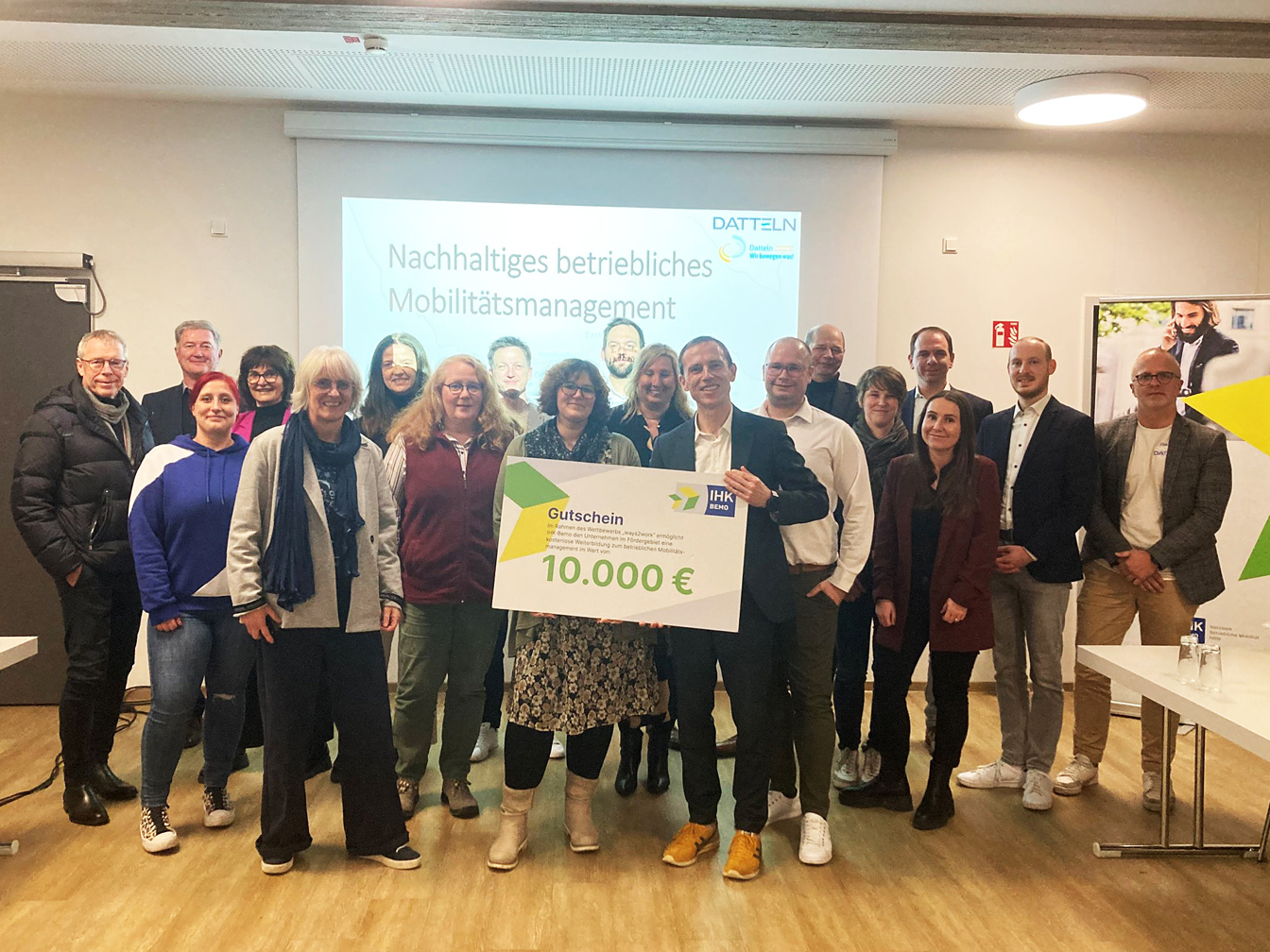 Foto: Gruppenbild mit Teilnehmer*innen, Vortragenden und Mitarbeiter*innen der Stadtverwaltung. Mobilitätskoordinatorin Nina Kuck und Stefan Peltzer präsentieren den Gutschein der IHK BEMO.