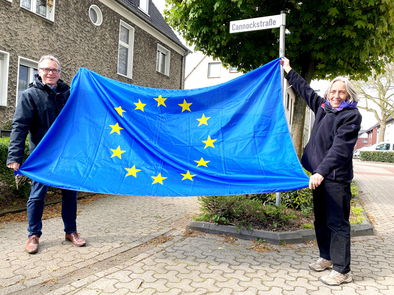 Bürgermeister André Dora und Rosemarie Schloßer mit einer Europafahne an der Cannockstraße