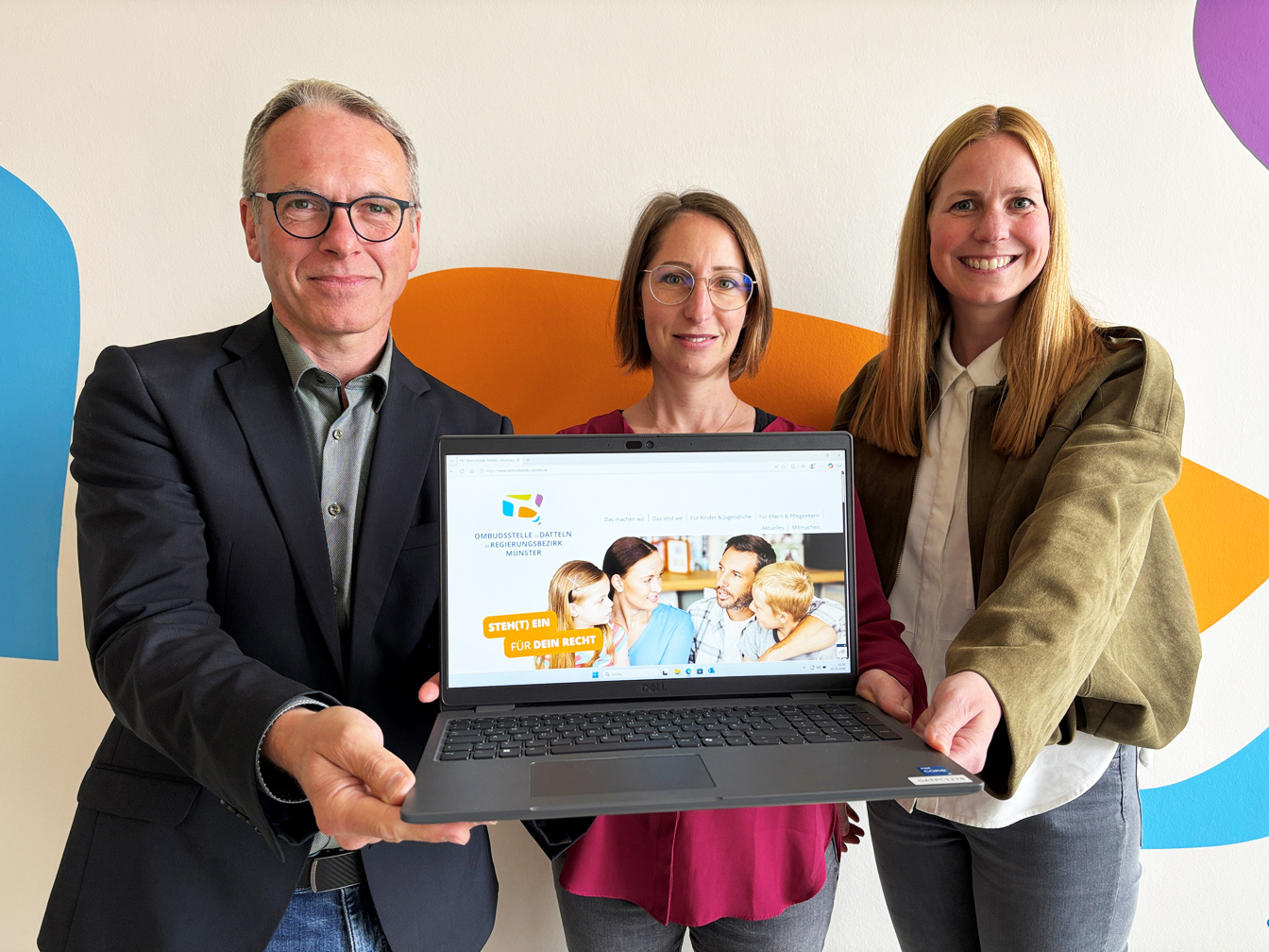 Drei Personen halten einen Laptop in die Kamera