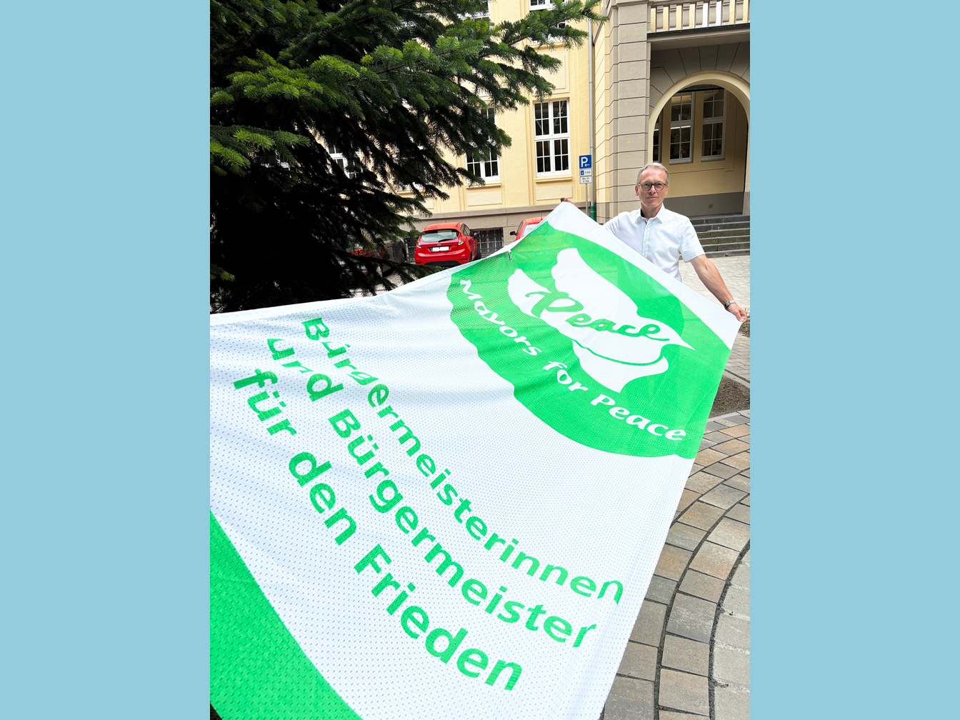 Bürgermeister André Dora mit der "Mayors for Peace"-Flagge vor dem Rathaus.