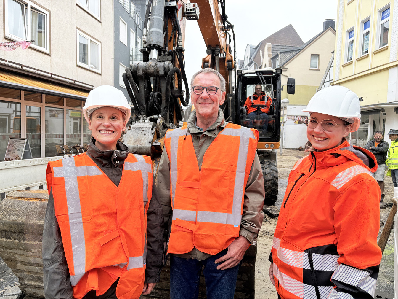 Drei Personen vor einem Bagger, in dem Bürgermeister Dora sitzt.