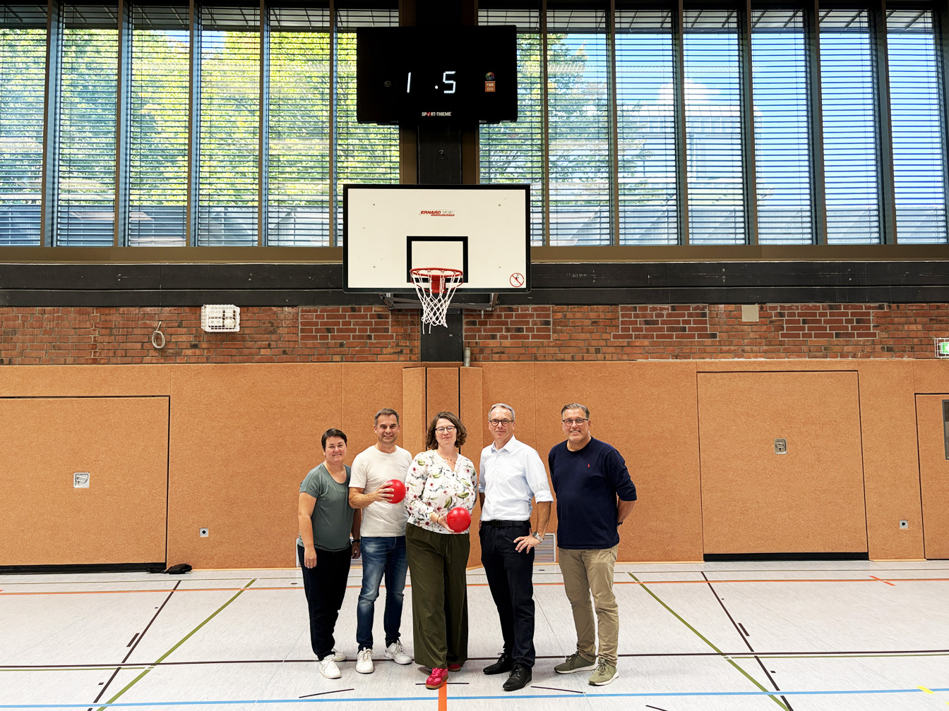 Bürgermeister und weitere Personen stehen in der Realschulturnhalle unter einem Basketballkorb