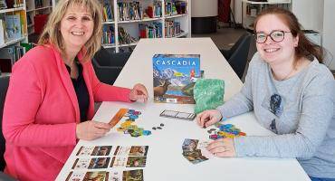 Sybille Schumacher (links) und Kiara Bender sitzen am  Tisch und spielen ein Gesellschaftsspiel in der Stadtbücherei