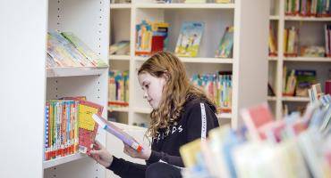 Ein Kind hat beim Stöbern im Bücherregal ein Buch in der Hand.