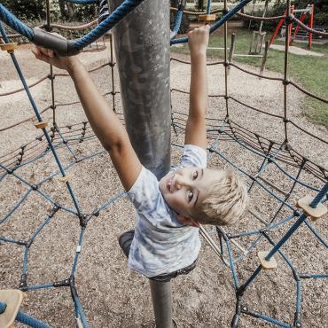 Das Bild zeigt einem auf dem Klettergerüst spielenden Jungen.