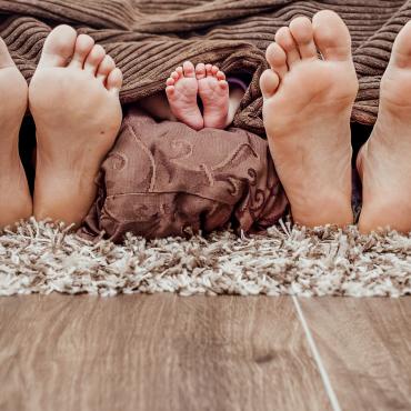 Das Bild zeigt jeweils die Füße eines Erwachsenen außen und die eines Kindes in der Mitte.