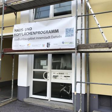 Das Bild zeigt eine Hausfassade mit Gerüst und dem Banner zum Haus- und Hofflächenprogramm.