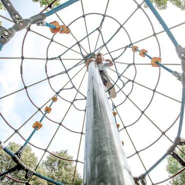 Das Bild zeigt einen spielenden Jungen auf einem hohen Klettergerüst.