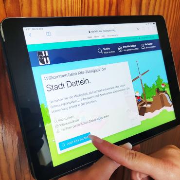 Das Bild zeigt eine Hand, die den Online-Kita-Navigator auf einem Tablet bedient.