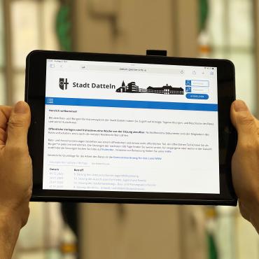 Das Bild zeigt zwei Hände, die ein Tablet halten, auf dem die Internetseite des Rats- und Bürgerinformationssystems aufgerufen ist. 