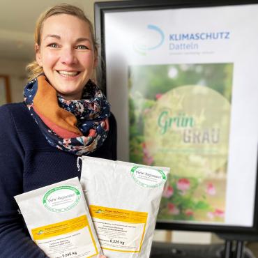 Das Bild zeigt Klimaschutzmanagerin Stefanie Pfitzmann, die zwei Saatgutmischungen in der Hand hält.