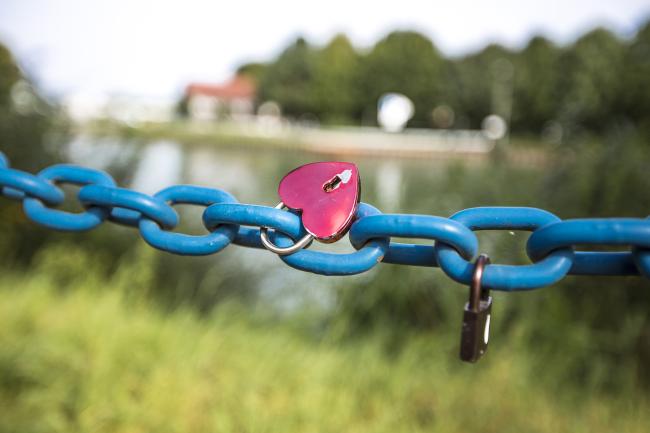Das Bild zeigt eine blaue Kette mit einem pinkfarbenen, herzförmigen Schloss.