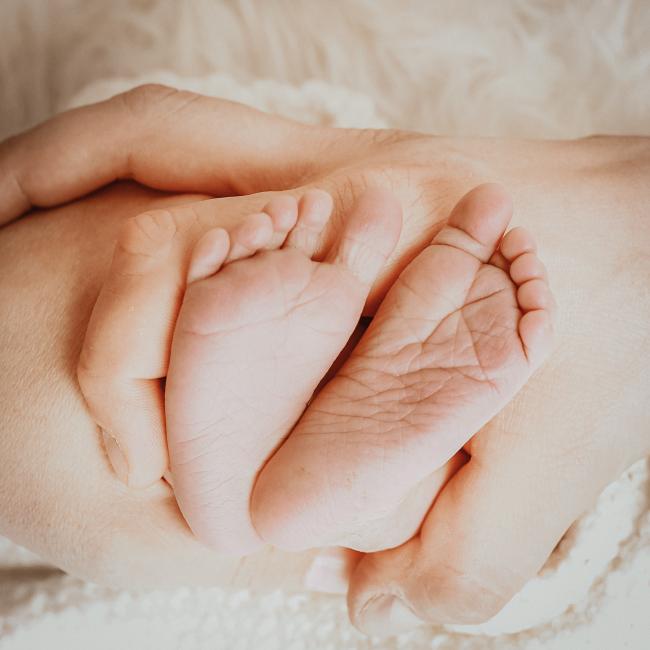 Das Bild zeigt Kinderfüße in den Händen der Eltern.