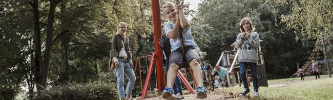 Das Bild zeigt Kinder auf einem Spielplatz, einer davon fährt mit der Seilbahn