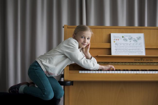 Das Bild zeigt ein Mädchen neben einem Klavier.