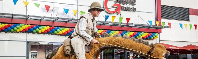 Das Bild zeigt einen Walking Act vor der StadtGalerie: ein Mann, der in einem Fantasietierkostüm steckt.