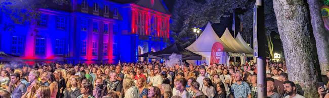Besucherinnen und Besucher, die vor der Bühne stehen; im Hintergrund das illuminierte Rathaus