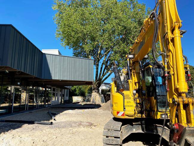 Links ist der Eingang zur Stadthalle zu sehen, rechts ein Bagger, dazwischen sehr viel Sand.