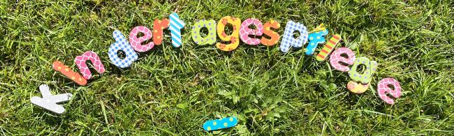 Das Wort "Kindertagespflege" ist mit einzelnen bunten Buchstaben auf einem Rasen gelegt worden.