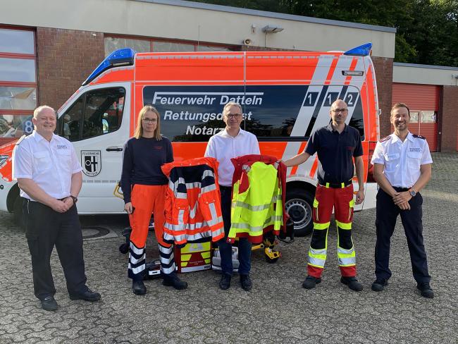 Von links sind zu sehen: Christan Wojtys (Leiter der Dattelner Feuerwehr), Lea Hölscher (Auszubildende zur Notfallsanitäterin), die symbolisch die bisherige Rettungsdienstkleidung an Bürgermeister André Dora übergibt, der die neue Rettungsdienstbekleidung an André Mühlen (Hauptbrandmeister) übergibt. Rechts im Bild ist Alexander Piel (Ausbilder bei der Dattelner Feuerwehr) zu sehen.