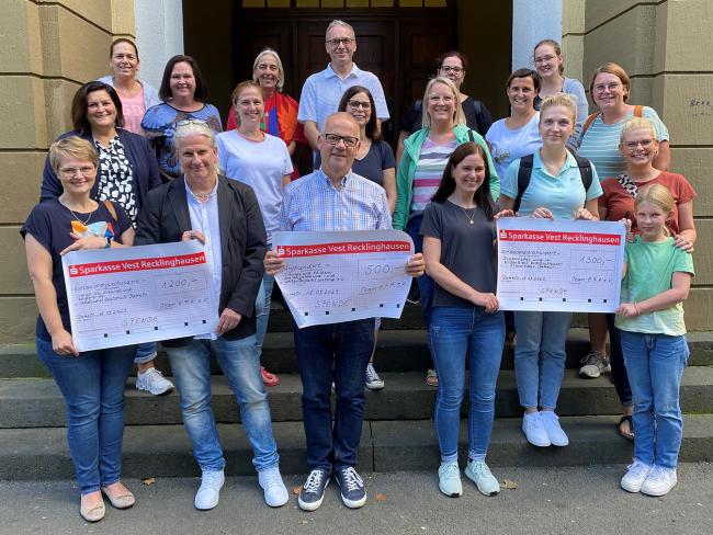 Mehrere Personen vom Team E.F.A., Vertreter*innen von Vereinen, die jeweils einen vergrößerten Scheck hochalten, die VHS-Leiterin Rosemarie Schloßer und Bürgermeister André Dora stehen auf der Rathaustreppe.  