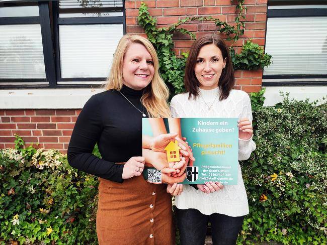 Jennifer Barnhofer (links) und Dana Tumbrink vor dem Familienbüro Süd mit einem Plakat zum Pflegekinderdienst in der Hand.