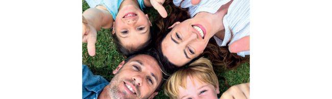 Vater, Mutter und zwei Kinder liegen auf einer Wiese, man sieht nur ihre Köpfe