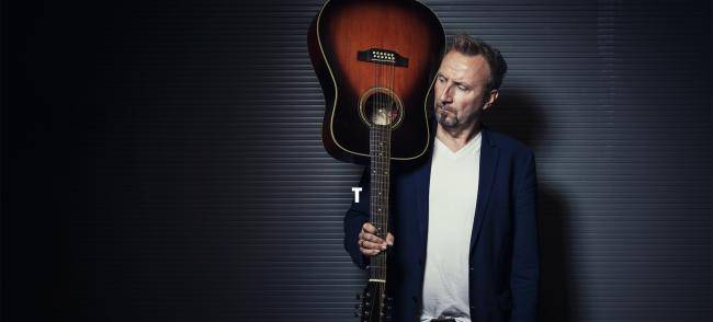 Helmut Sanftenschneider mit Hemd und Sakko und Gitarre in der Hand