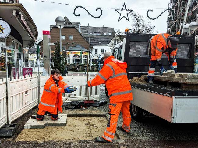 Für die Umgestaltung der Fußgängerzone verlegen drei Mitarbeiter Musterflächen für Steine in der Fußgängerzone.