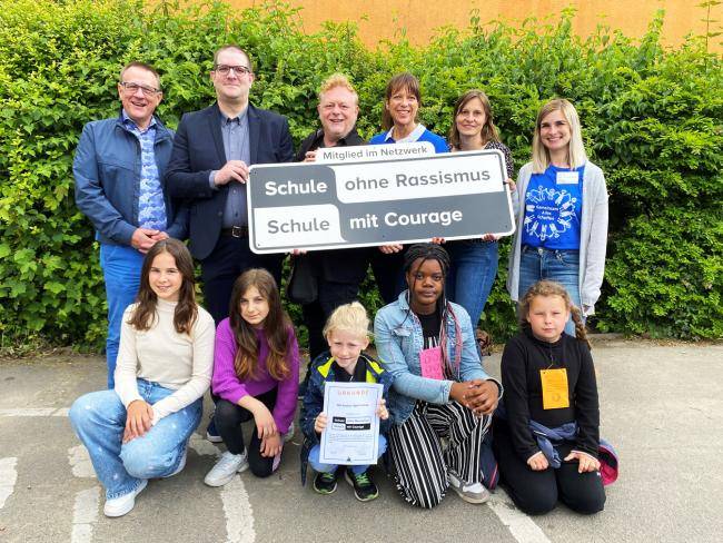 Schüler*innen der Gustav-Adolf-Schule zeigen das Schild "Schule ohne Rassismus - Schule mit Courage" unter anderem mit dem Dezernenten der Stadtverwaltung Peter Wenzel und Konrektorin Sandra Böcker  