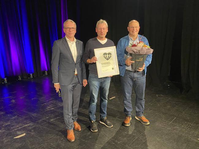 Reinhard Jaisfeld (r.), Ehemann von Sylvia Jaisfeld, und Diethard Klaßen (m.), Mitbegründer des Chores InTak nehmen den Ehrenamtspreis für Sylvia Jaisfeld von Bürgermeister AndréDora entgegen