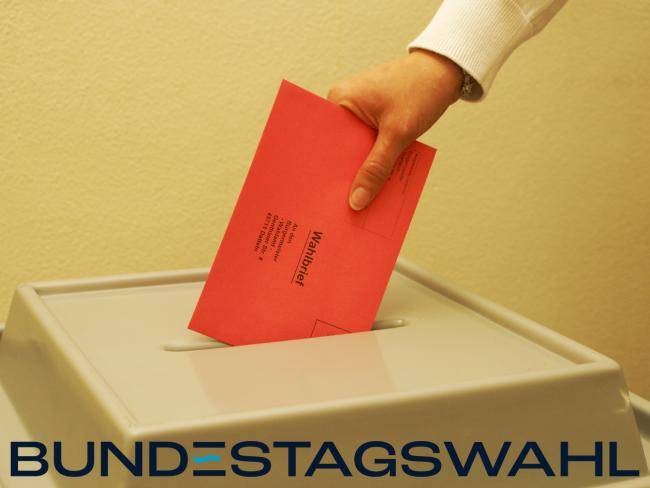 Wahlbrief wird in eine Wahlurne gesteckt.