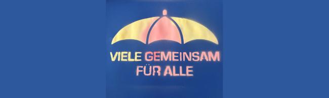 Unter einem aufgesprühten Regenschirm steht der Text "Viele gemeinsam für alle"