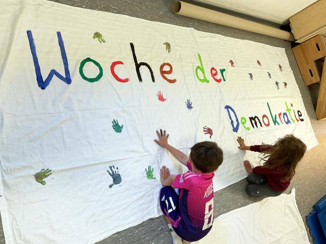 Kinder der Dependance der Städtischen Bewegungskita in der Berliner Straße gestalten ein großes Tuch mit Handabdrücken 