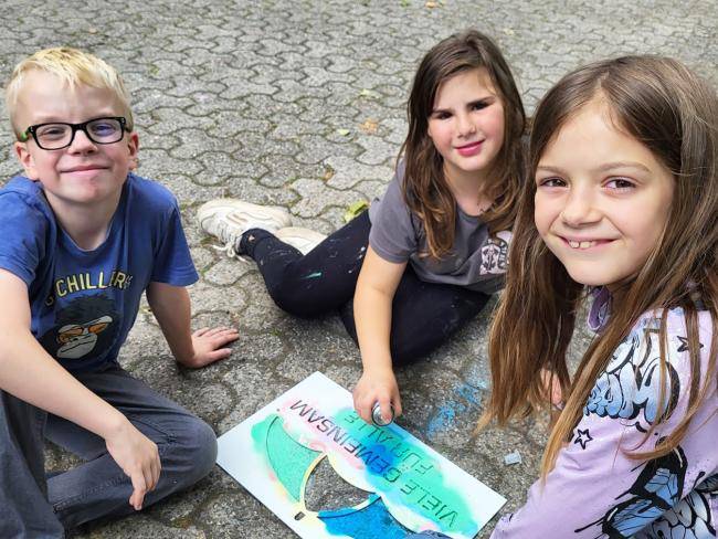 Kinder mit der Schablone "Viele gemeinsam für alle" zum Auftakt der "Woche der Demokratie" am Friedenslabor am Stadtbad