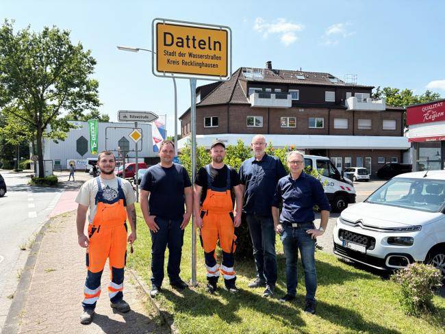 Auf dem Foto sind zu sehen (v. l.): Ilias Veziridis (KSD), Marvin Müller (KSD), Mike Westhoff (KSD), Ralf Feldhaus (Fachdienstleiter Verkehrsangelegenheiten) und Bürgermeister André Dora - dahinter das neue Ortseingangsschild mit der Bezeichnung "Datteln - Stadt der Wasserstraßen"