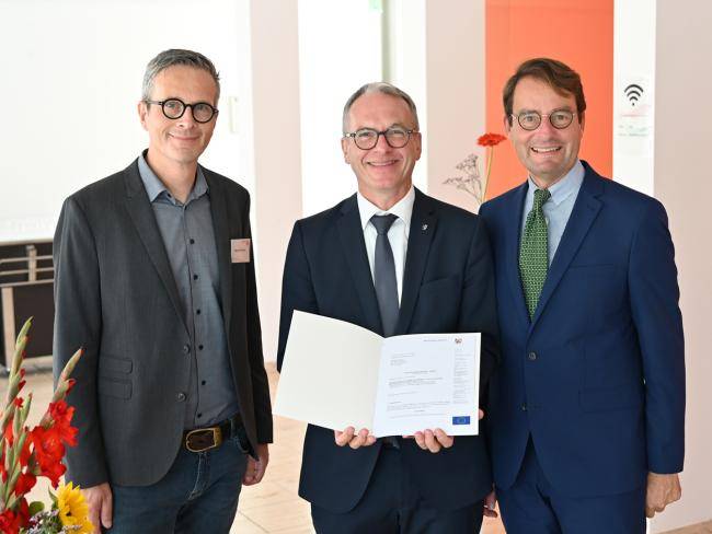 Bürgermeister André Dora mit Förderbescheid für die Fortsetzung des Innenstadtumbaus. Rechts ist Regierungspräsident Andreas Bothe zu sehen, links Stephan Kemper vom Dezernat Städtebau.