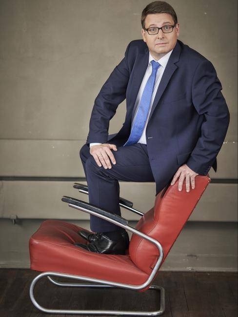 Das Bild zeigt den Künstler Kai Magnus Sting auf einem roten Stuhl