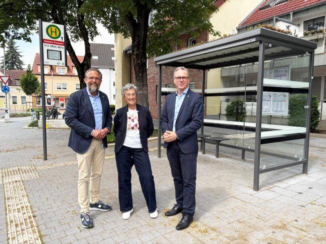 Drei Personen stehen an der Haltestelle "Datteln Postamt" und stellen das Projekt "Mobil ohne Auto" vor.