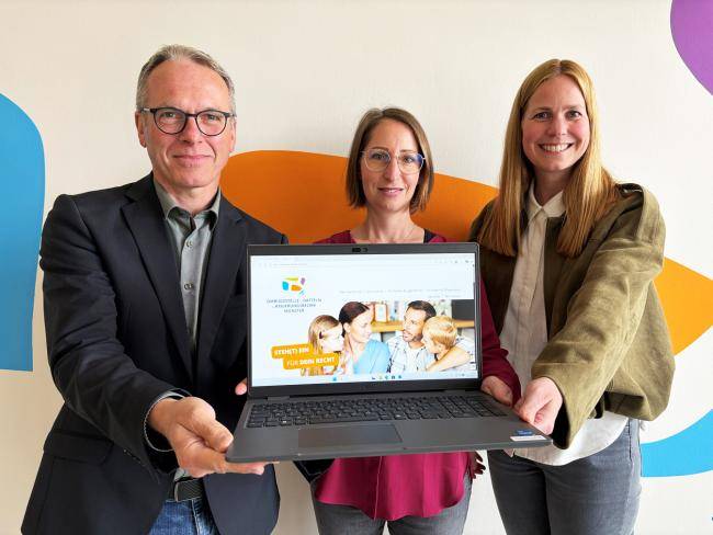 Drei Personen halten einen Laptop in die Kamera