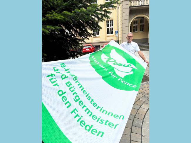 Bürgermeister André Dora mit der "Mayors for Peace"-Flagge vor dem Rathaus.